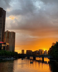 Buildings by river against sky during sunset