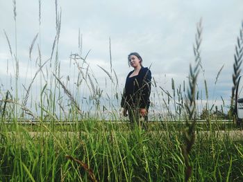 Young woman standing on field against sky