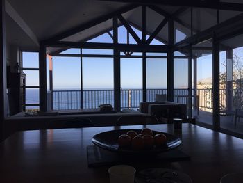 Chairs and table by sea against sky seen through window