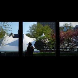 Silhouette people by glass window against sky