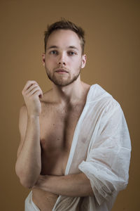 Portrait of confident young male model standing against brown background