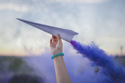 Close-up of hand holding paper against sky