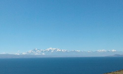 Scenic view of sea and snowcapped mountains against clear blue sky