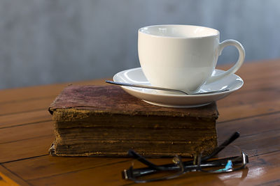 Close-up of coffee cup with book and eyeglasses on wooden table