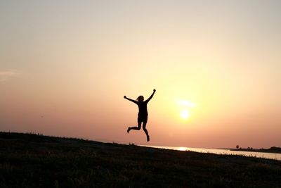 Silhouette man jumping on field against sky during sunset