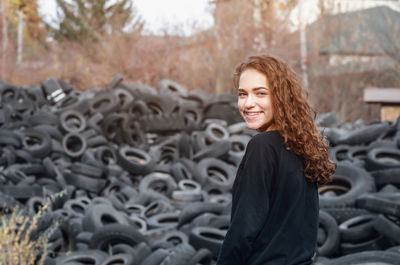Curly girl with beaming smile on the background of pile of tires. ecological problems.
