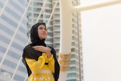 Low angle view of young woman wearing hijab while looking away in city