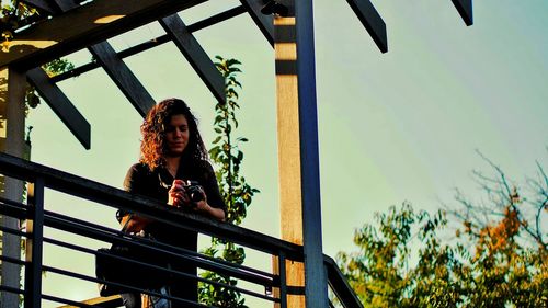 Low angle view of young woman photographing while standing in balcony