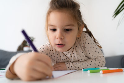 Portrait of cute preschooler child girl drawing with pencils at home while sitting in front