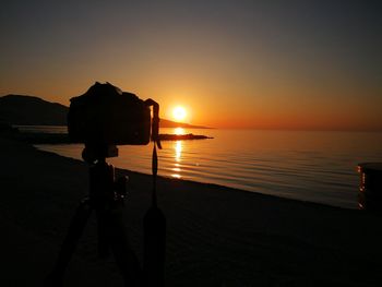 Silhouette person photographing sea against sky during sunset