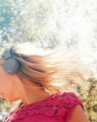 Close-up of young woman listening music while standing against trees at park