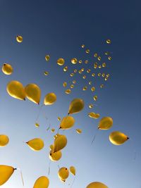 Low angle view of yellow balloons flying against blue sky