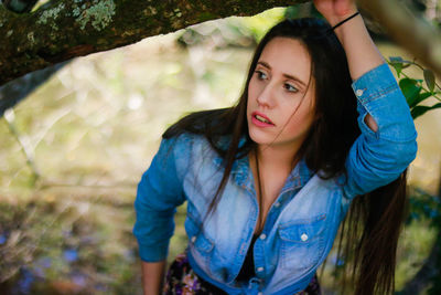 Woman looking away while standing against tree