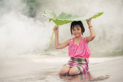 Portrait of girl holding leaf while kneeling on field during rainfall