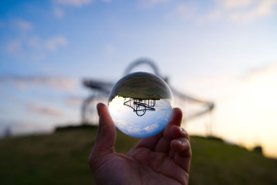 Close-up of hand holding crystal ball against roller coaster during sunset