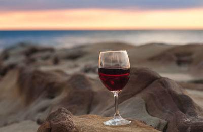 Close-up of wineglass on table against sea during sunset