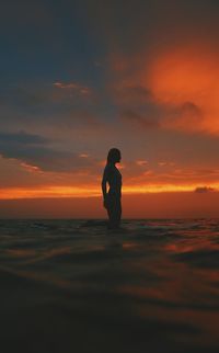 Silhouette young woman surfing on sea against cloudy sky during sunset