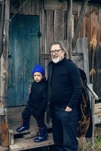 Grandson in a blue hat and boots with a grandfather in a sheepskin coat stand 