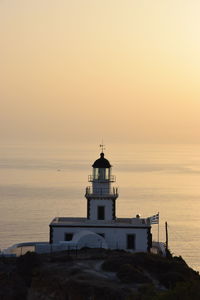 Lighthouse by sea against sky during sunset