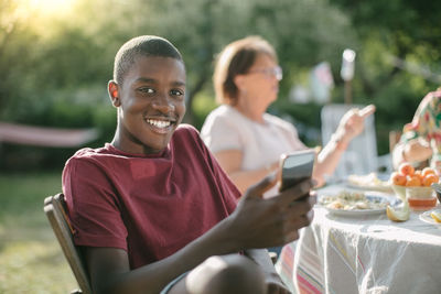 Portrait of smiling boy using mobile phone in backyard during garden party