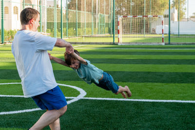 Father spinning son on sports ground. view from behind