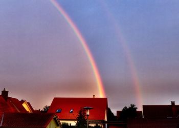 Low angle view of rainbow over buildings against cloudy sky