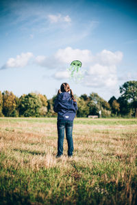 Rear view of girl flying kite on land against sky