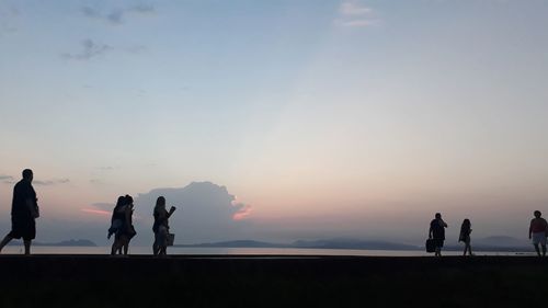 Silhouette people at beach against sky during sunset