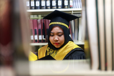 Young woman wearing graduation gown in library