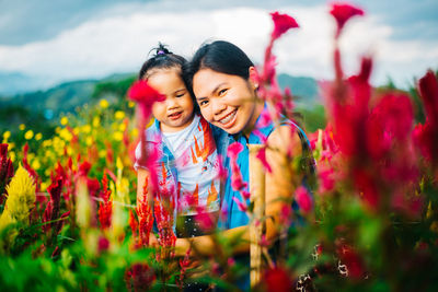 Portrait of happy mother and daughter with flowers on field against sky