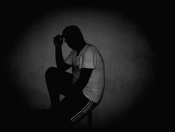 Side view of man sitting on chair against wall