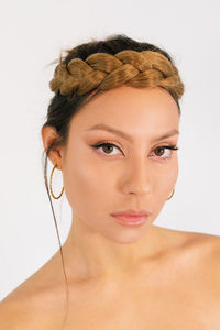 Beautiful young female model with elegant braided hairstyle and makeup and with golden hoop earrings against white background looking at camera