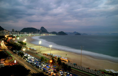 High angle view of illuminated city by sea against sky