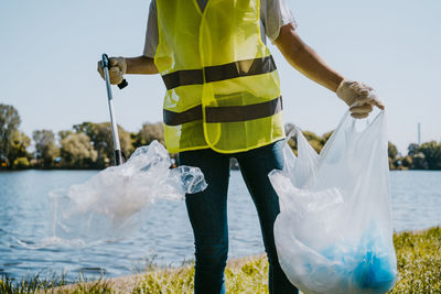 Midsection of young male environmentalist picking up plastic against lake