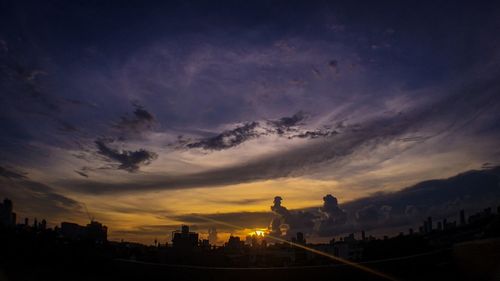 Silhouette of buildings against cloudy sky at sunset