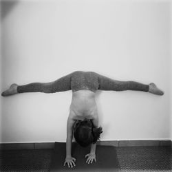 Shirtless girl doing split against wall at home