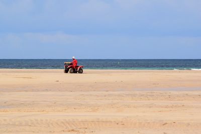 Man riding quadbike at beach against blue sky