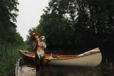 Young man stands in shallow river next to his canoe with a dog. adventurous active rest concept