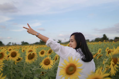 Portrait of young woman with arms raised against sky