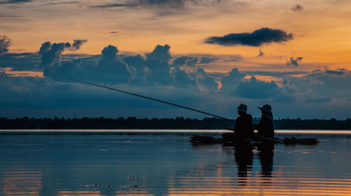 Silhouette men fishing in lake against sky during sunset