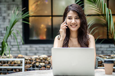 Smiling young woman using phone at cafe