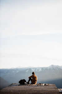 Rear view of people sitting on mountain against sky