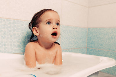 Topless girl with mouth open looking away while sitting in bathtub at home