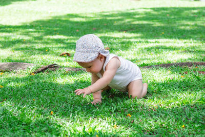 Portrait of little baby girl in white clothing and panama. child tries to crawl on grass in park. 