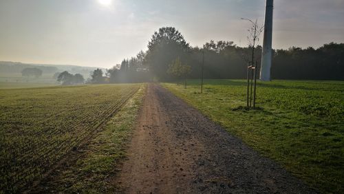 Road amidst field against sky during foggy weather