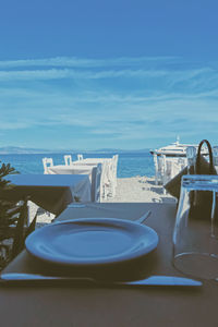 Empty chairs and tables at beach against blue sky