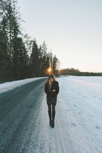 Full length of woman standing on snow covered road during sunset