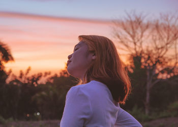 Portrait of young woman looking away against sky during sunset