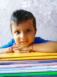 Portrait of cute boy with stacked books sitting against wall at home