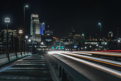 Light trails on street amidst illuminated buildings in city at night